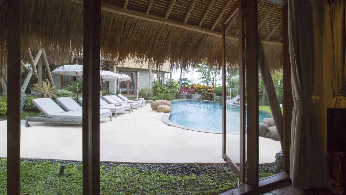 Spacious open-plan Bali villa living area with white sofas, rustic wooden coffee table, bamboo ceiling, tropical plants, and Buddha statue. - Bali Villas