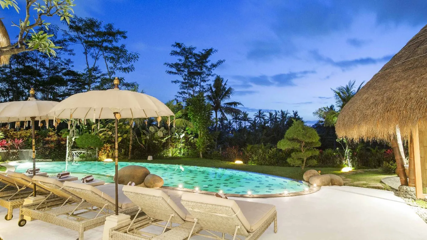 Spacious open-plan Bali villa living area with white sofas, rustic wooden coffee table, bamboo ceiling, tropical plants, and Buddha statue. - Bali Villas