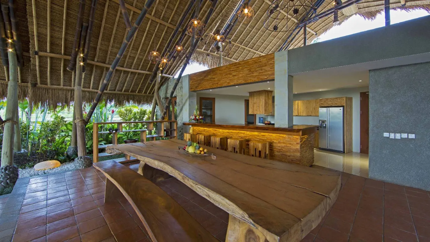 Spacious open-plan Bali villa living area with white sofas, rustic wooden coffee table, bamboo ceiling, tropical plants, and Buddha statue. - Bali Villas