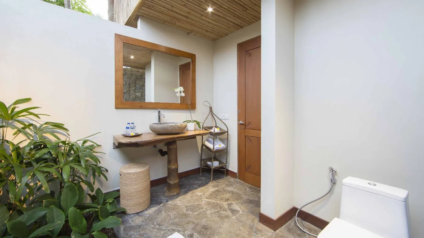 Spacious open-plan Bali villa living area with white sofas, rustic wooden coffee table, bamboo ceiling, tropical plants, and Buddha statue. - Bali Villas