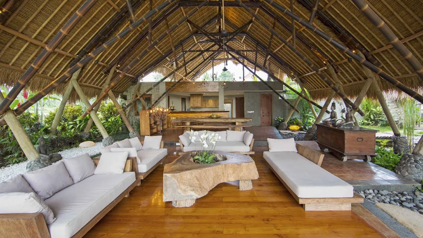 Spacious open-plan Bali villa living area with white sofas, rustic wooden coffee table, bamboo ceiling, tropical plants, and Buddha statue. - Bali Villas