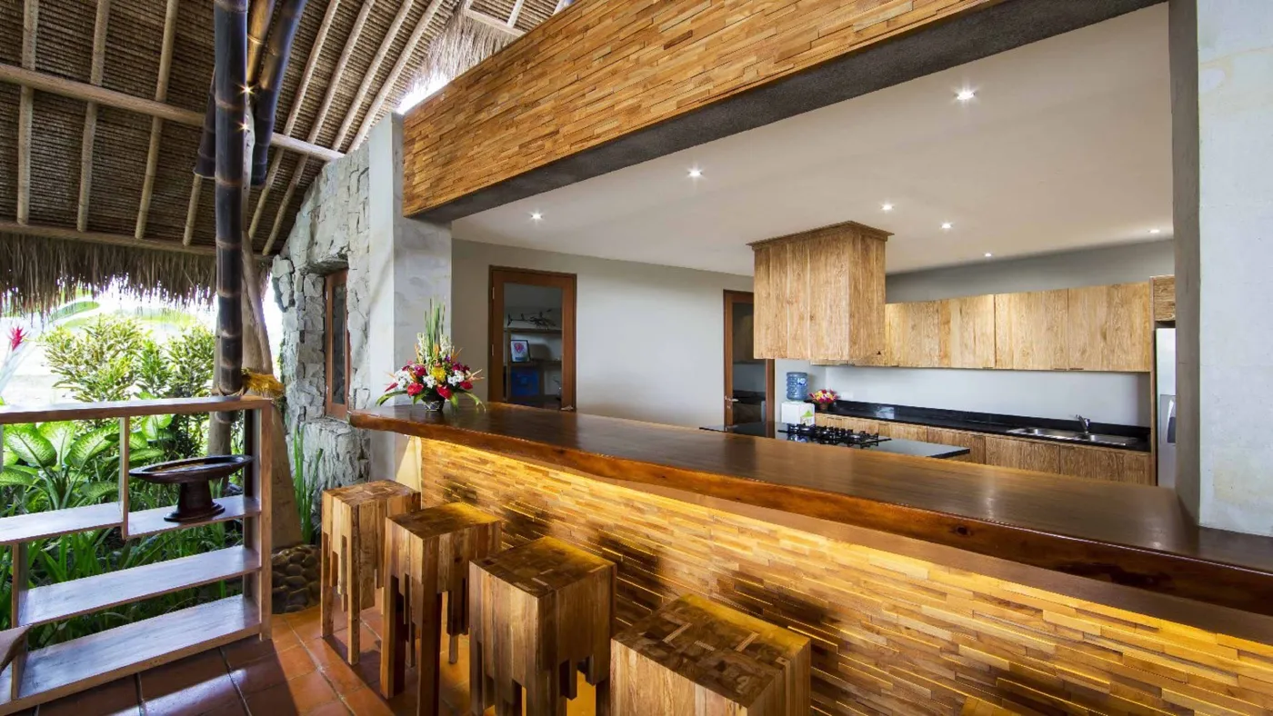 Spacious open-plan Bali villa living area with white sofas, rustic wooden coffee table, bamboo ceiling, tropical plants, and Buddha statue. - Bali Villas