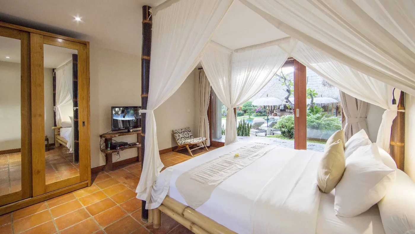 Spacious open-plan Bali villa living area with white sofas, rustic wooden coffee table, bamboo ceiling, tropical plants, and Buddha statue. - Bali Villas