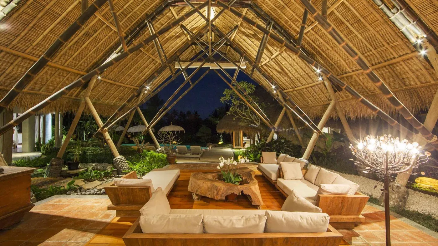 Spacious open-plan Bali villa living area with white sofas, rustic wooden coffee table, bamboo ceiling, tropical plants, and Buddha statue. - Bali Villas