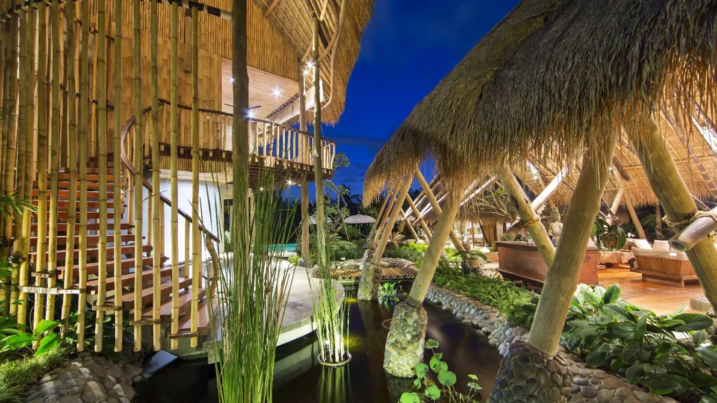 Spacious open-plan Bali villa living area with white sofas, rustic wooden coffee table, bamboo ceiling, tropical plants, and Buddha statue. - Bali Villas