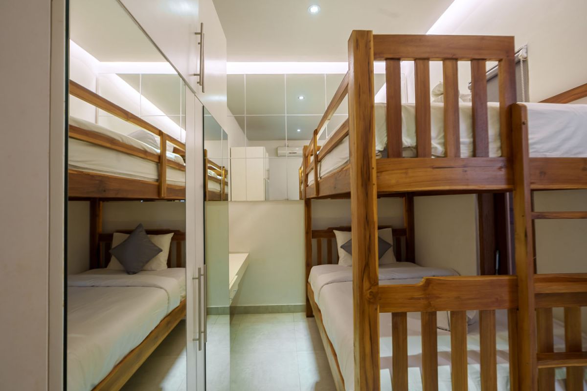 Modern living room with wooden wall panels, orange patterned sofa, Netflix on wall-mounted TV, abstract wall art, and potted plants. - Bali Villas