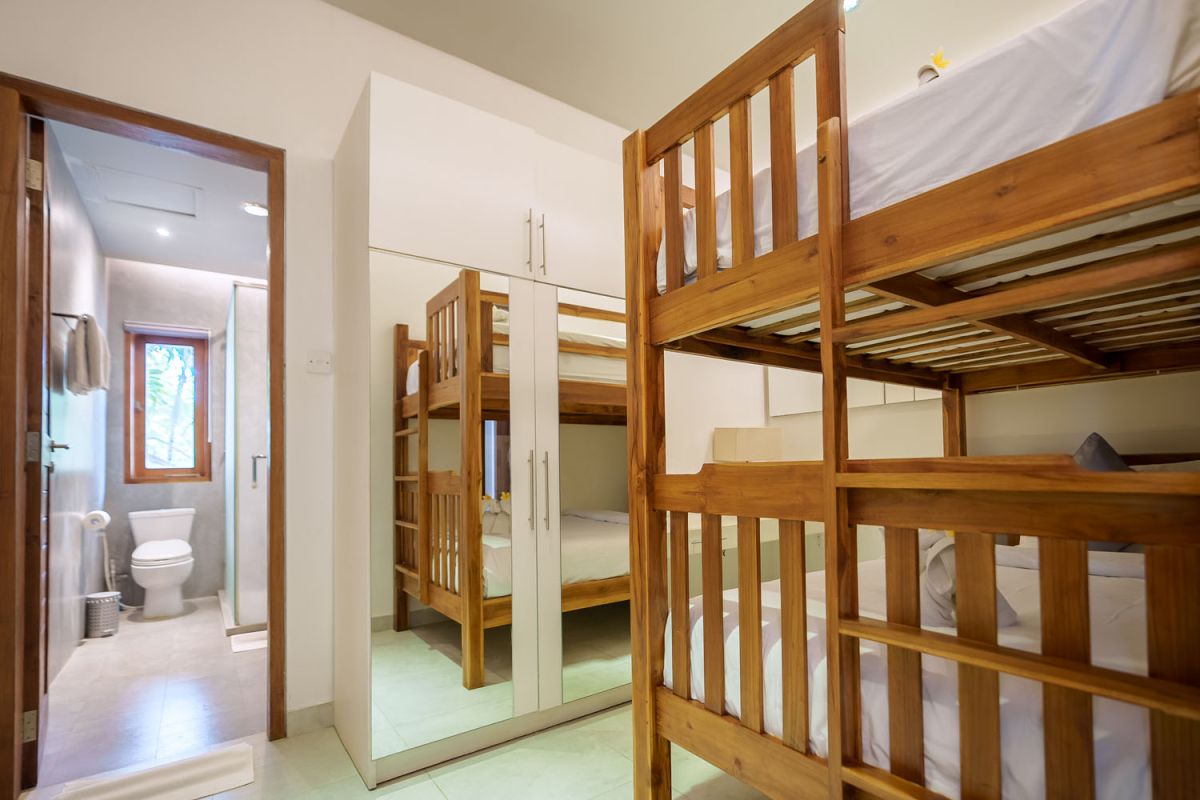 Modern living room with wooden wall panels, orange patterned sofa, Netflix on wall-mounted TV, abstract wall art, and potted plants. - Bali Villas