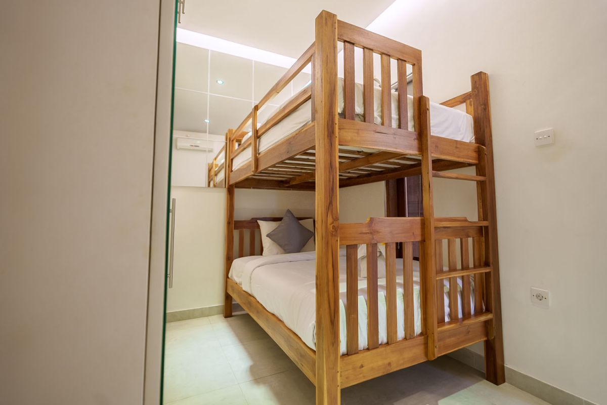 Modern living room with wooden wall panels, orange patterned sofa, Netflix on wall-mounted TV, abstract wall art, and potted plants. - Bali Villas