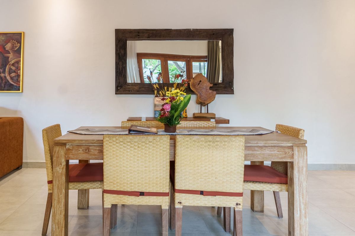 Modern living room with wooden wall panels, orange patterned sofa, Netflix on wall-mounted TV, abstract wall art, and potted plants. - Bali Villas