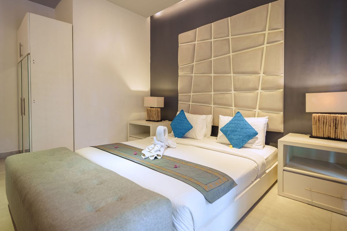 Modern living room with wooden wall panels, orange patterned sofa, Netflix on wall-mounted TV, abstract wall art, and potted plants. - Bali Villas