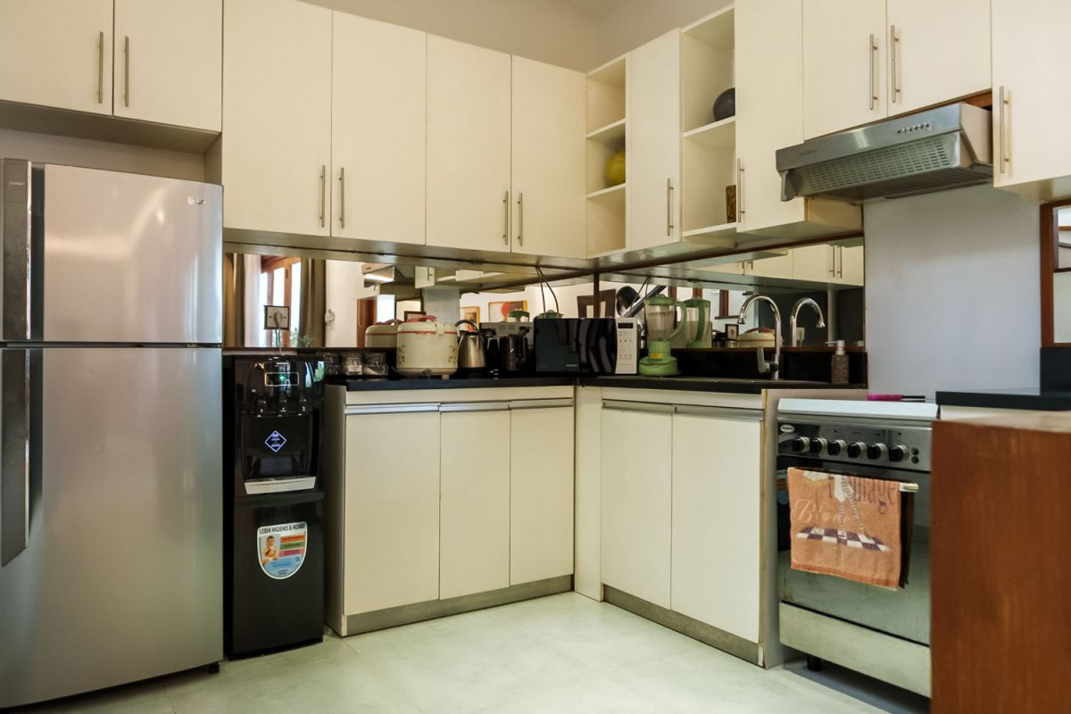 Modern living room with wooden wall panels, orange patterned sofa, Netflix on wall-mounted TV, abstract wall art, and potted plants. - Bali Villas