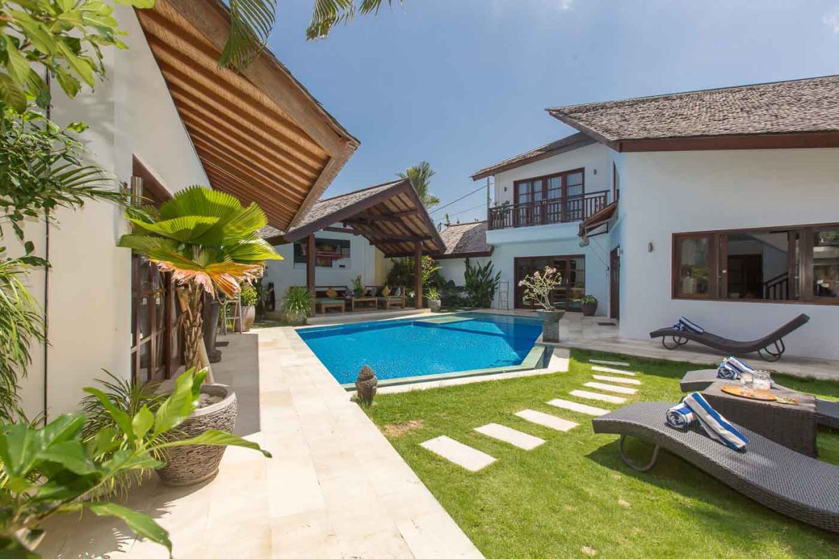 Luxurious Balinese bathroom with petal-filled stone bathtub, rain shower, wooden beamed ceiling, and tropical accents. - Bali Villas