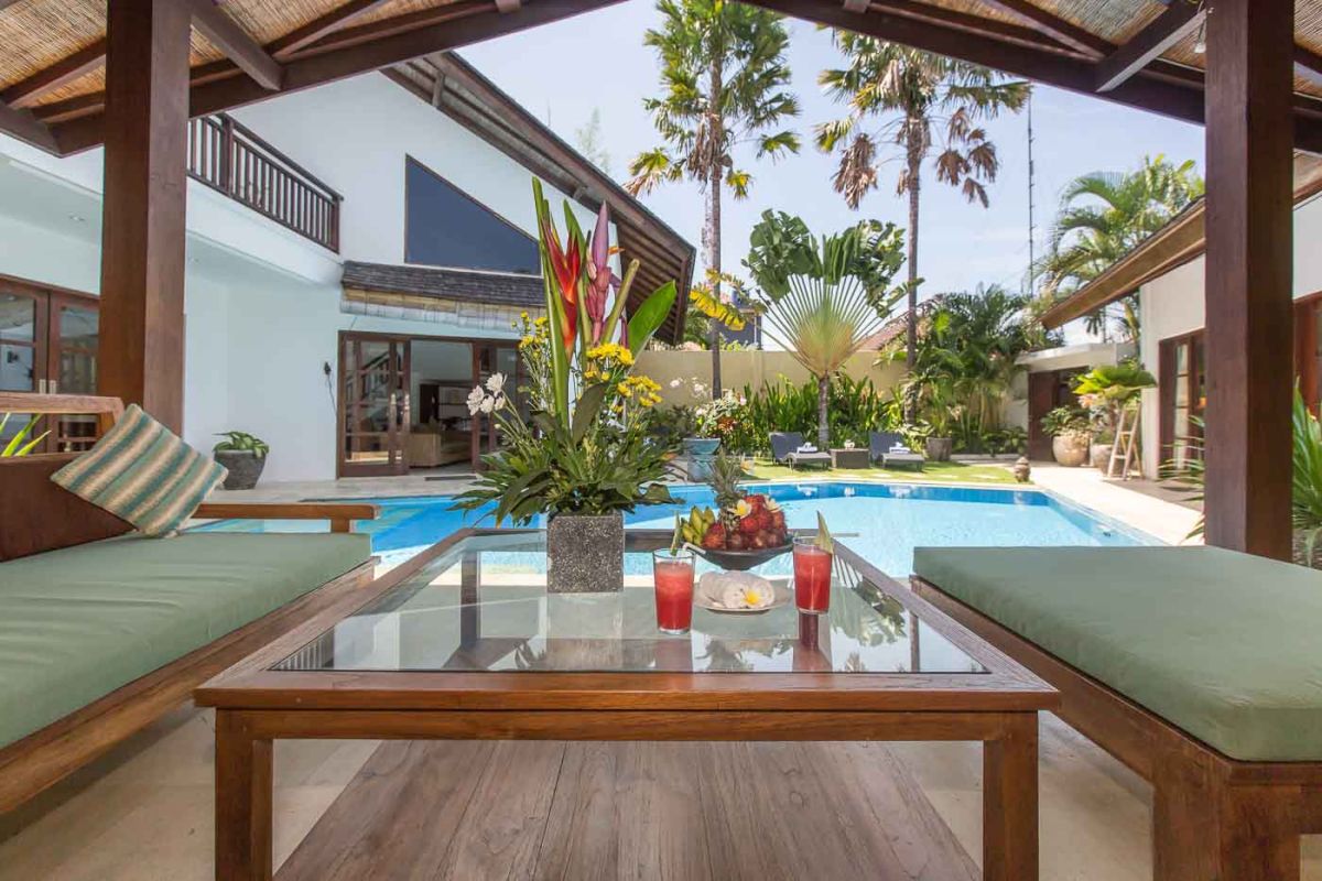 Luxurious Balinese bathroom with petal-filled stone bathtub, rain shower, wooden beamed ceiling, and tropical accents. - Bali Villas