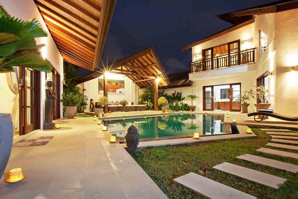 Luxurious Balinese bathroom with petal-filled stone bathtub, rain shower, wooden beamed ceiling, and tropical accents. - Bali Villas