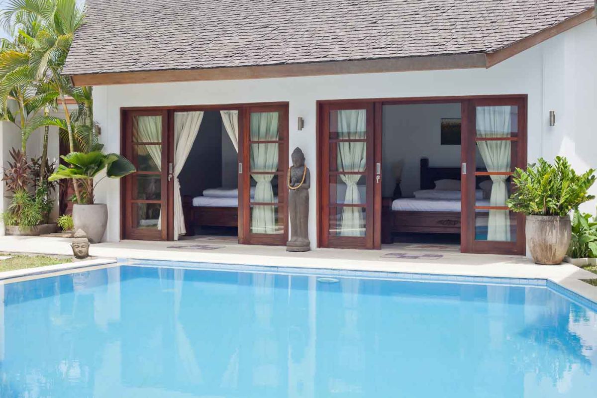 Luxurious Balinese bathroom with petal-filled stone bathtub, rain shower, wooden beamed ceiling, and tropical accents. - Bali Villas