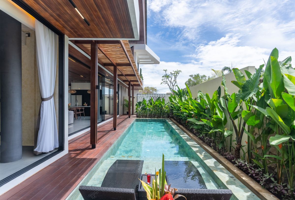 Modern wooden pool table in a spacious tropical living room with large windows, plants, and cozy seating. - Bali Villas