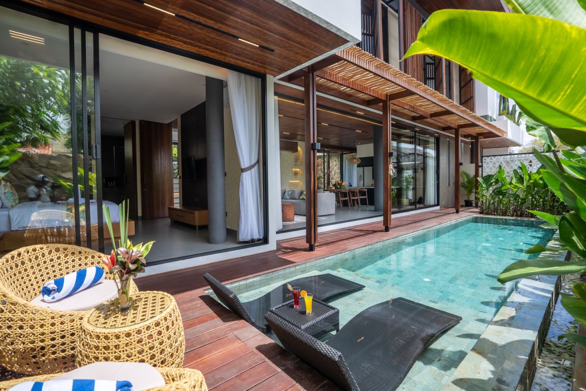 Modern wooden pool table in a spacious tropical living room with large windows, plants, and cozy seating. - Bali Villas