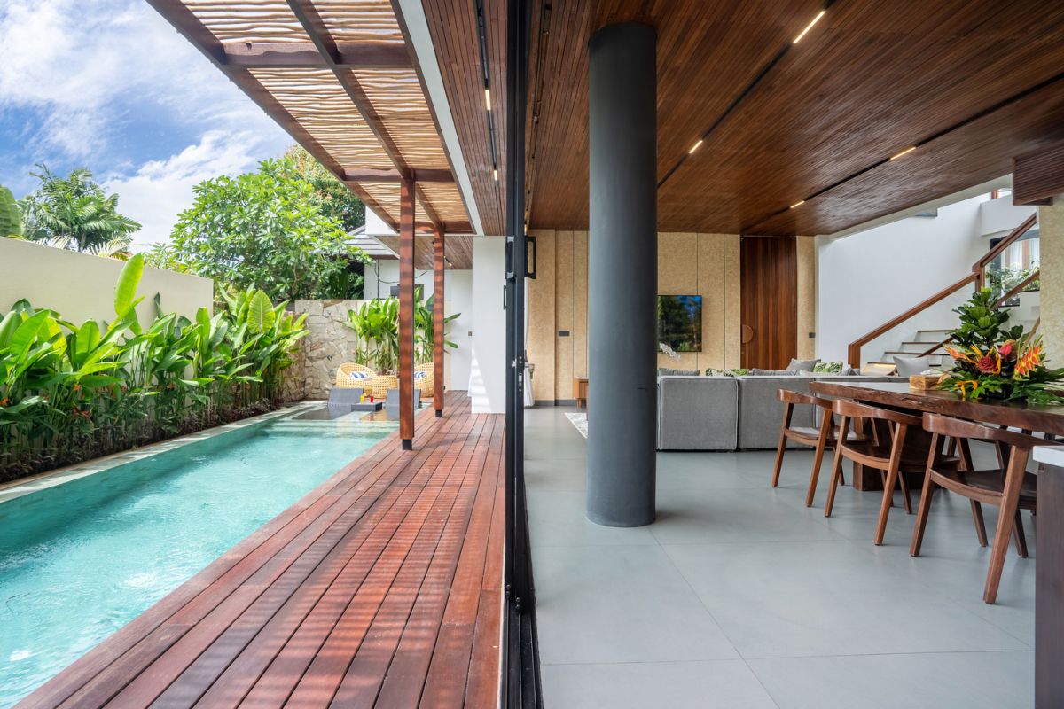 Modern wooden pool table in a spacious tropical living room with large windows, plants, and cozy seating. - Bali Villas