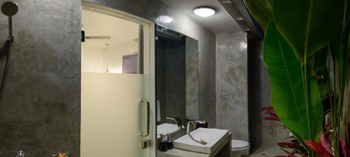 Luxurious open-air Balinese villa featuring an infinity pool, gray lounge seating, wooden dining table, and tropical plants under a blue sky. - Bali Villas