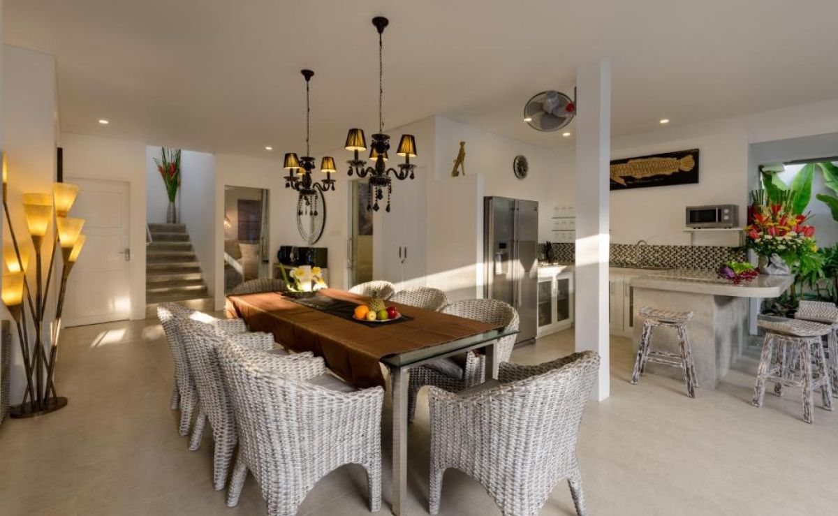 Luxurious open-air Balinese villa featuring an infinity pool, gray lounge seating, wooden dining table, and tropical plants under a blue sky. - Bali Villas