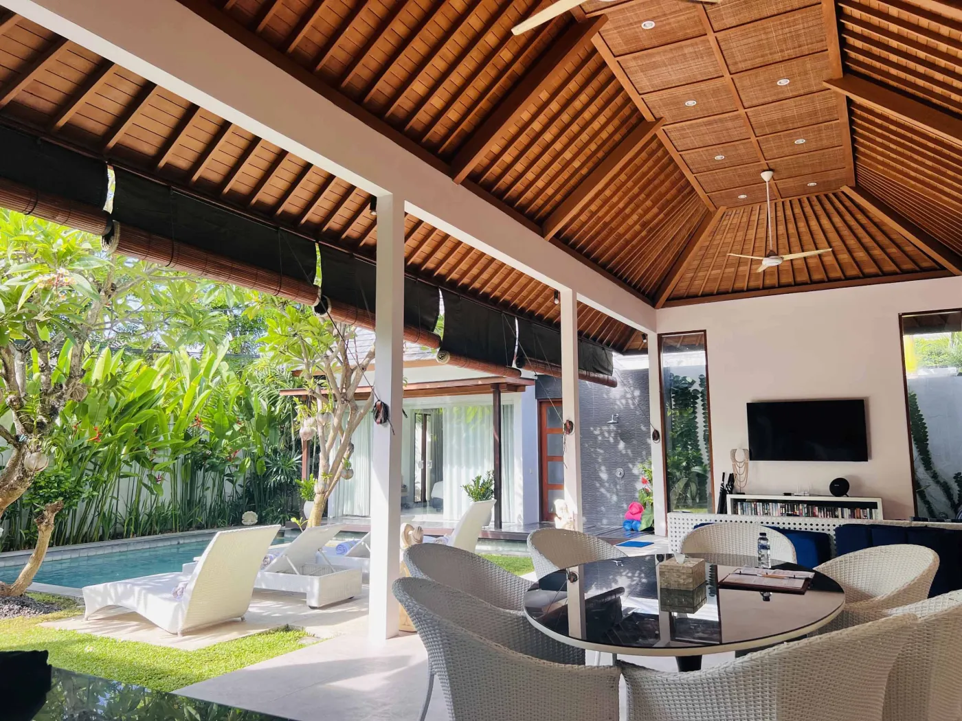 Serene Balinese villa pool with turquoise water, white lounge chairs, frangipani trees, and lush tropical greenery under a blue sky. - Bali Villas