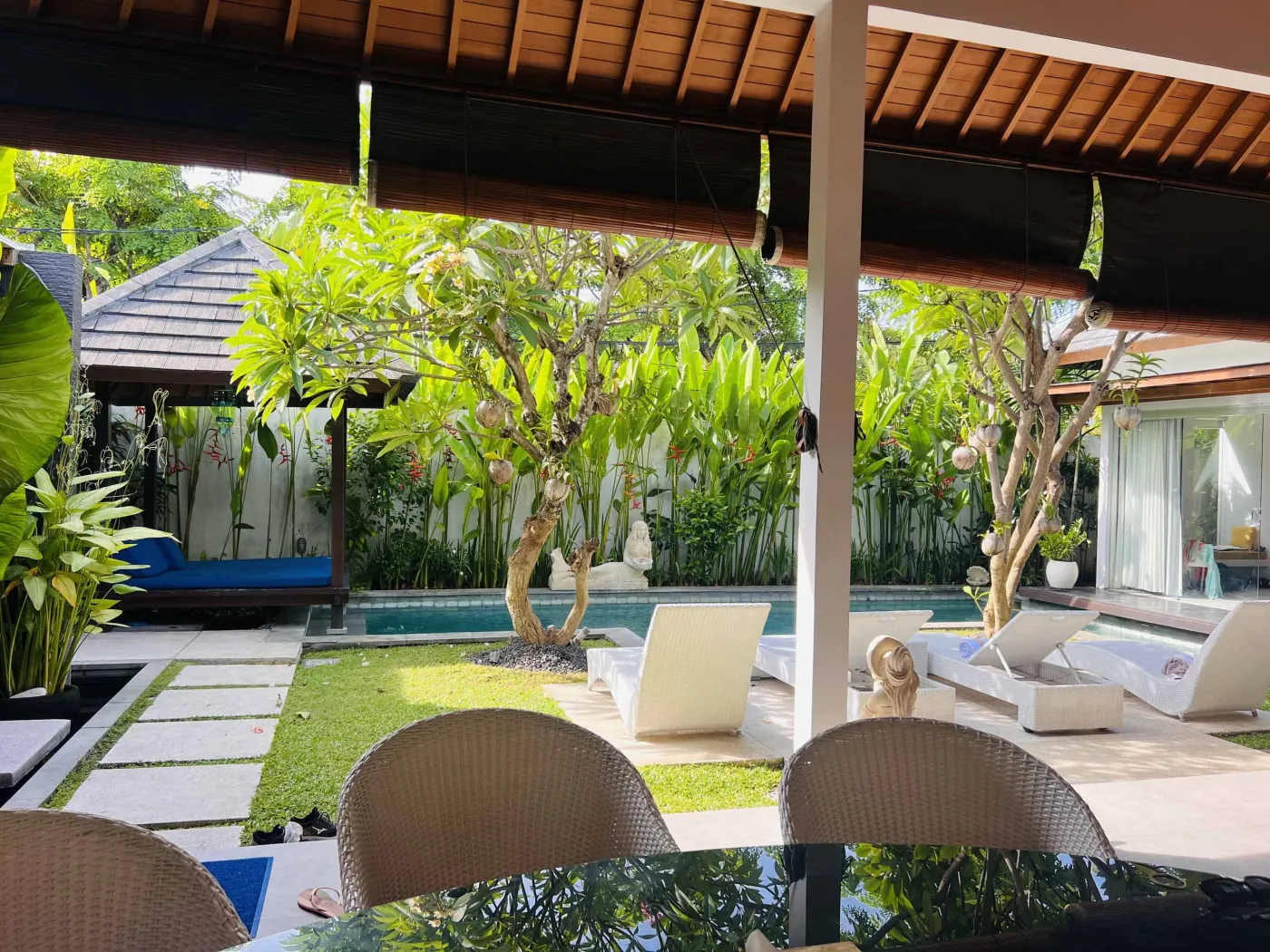 Serene Balinese villa pool with turquoise water, white lounge chairs, frangipani trees, and lush tropical greenery under a blue sky. - Bali Villas
