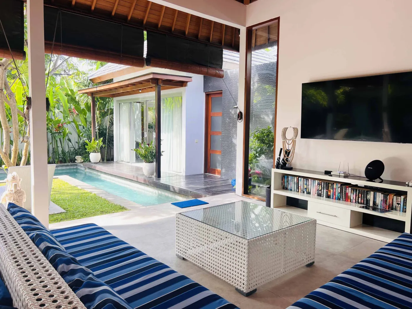 Serene Balinese villa pool with turquoise water, white lounge chairs, frangipani trees, and lush tropical greenery under a blue sky. - Bali Villas