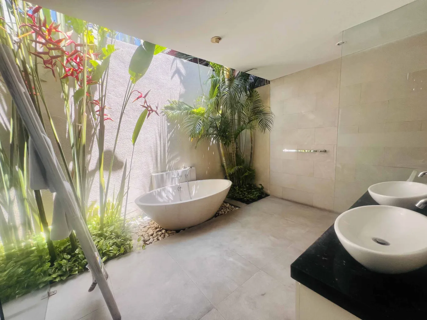 Serene Balinese villa pool with turquoise water, white lounge chairs, frangipani trees, and lush tropical greenery under a blue sky. - Bali Villas