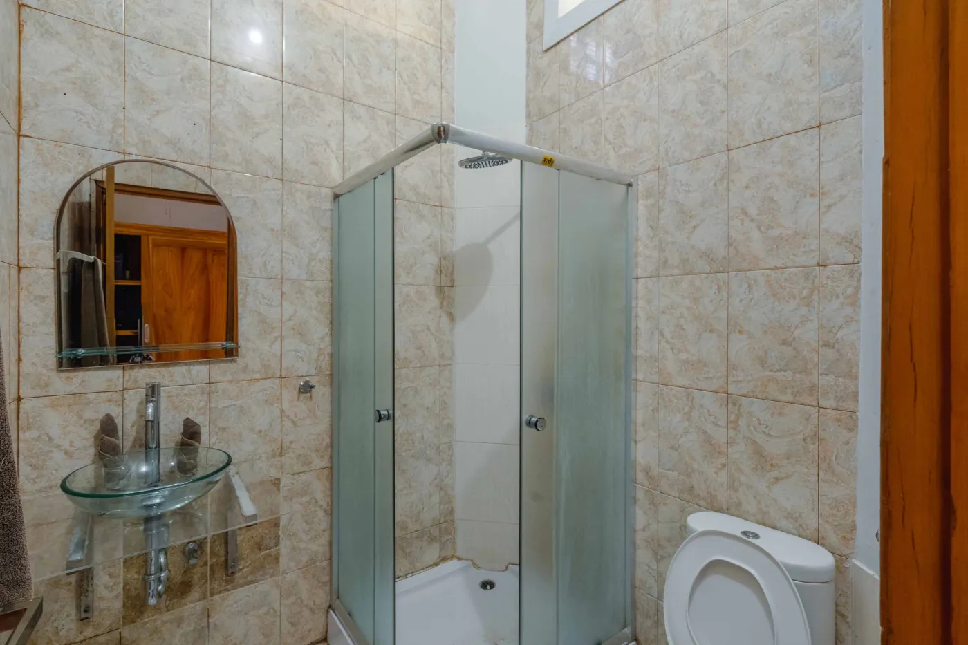 Rustic Balinese kitchen with wooden cabinets, blue range hood, mosaic tiled backsplash, black fridge, and ceiling fan. - Bali Villas