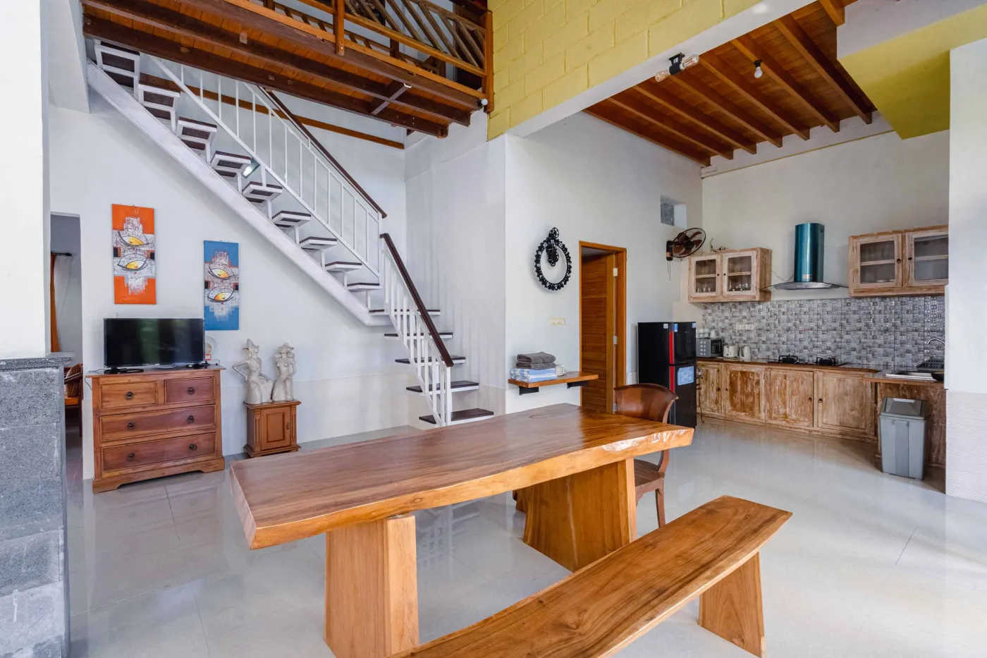 Rustic Balinese kitchen with wooden cabinets, blue range hood, mosaic tiled backsplash, black fridge, and ceiling fan. - Bali Villas