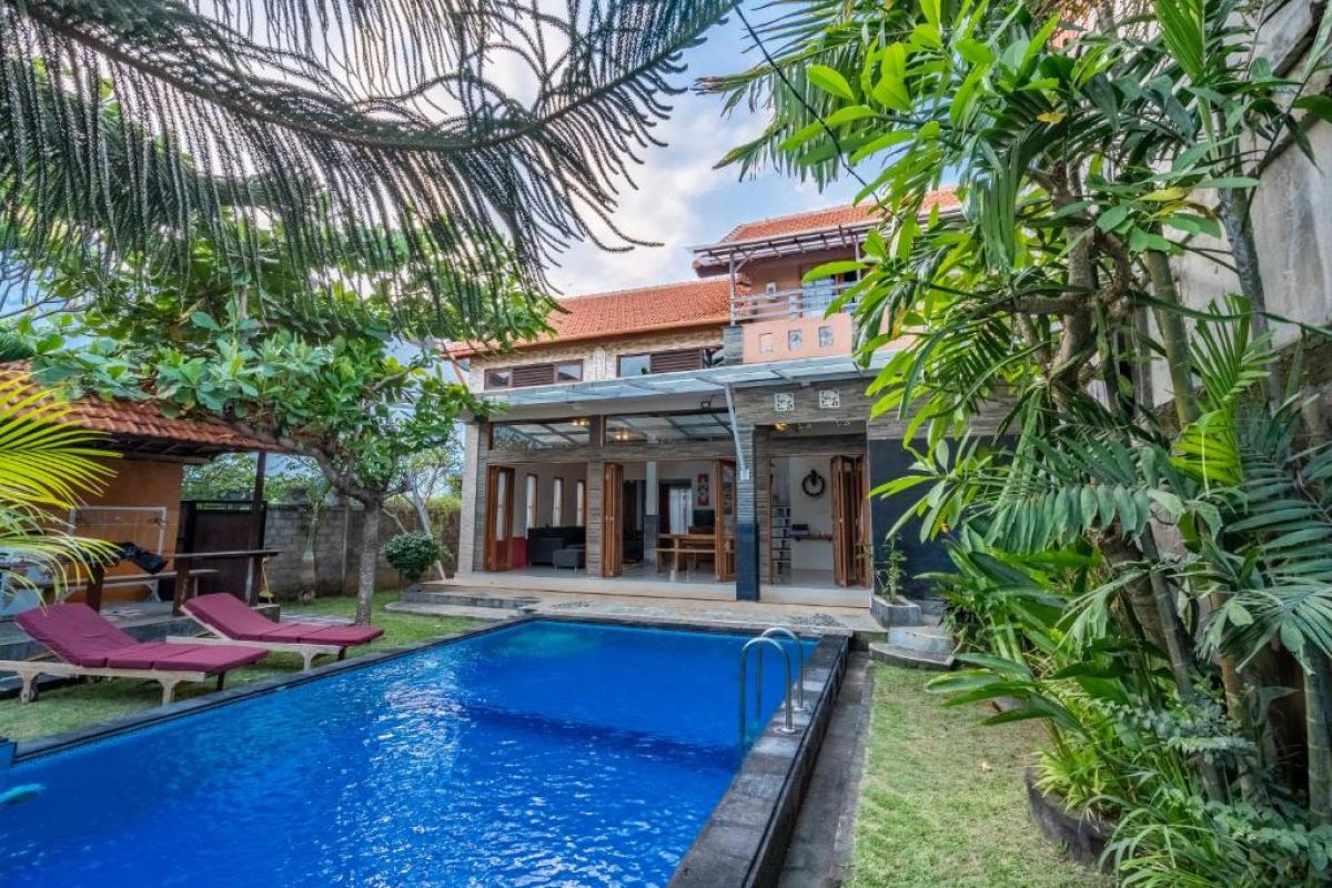 Luxury Balinese villa with blue infinity pool, red lounge chairs, and lush tropical gardens. - Bali Villas