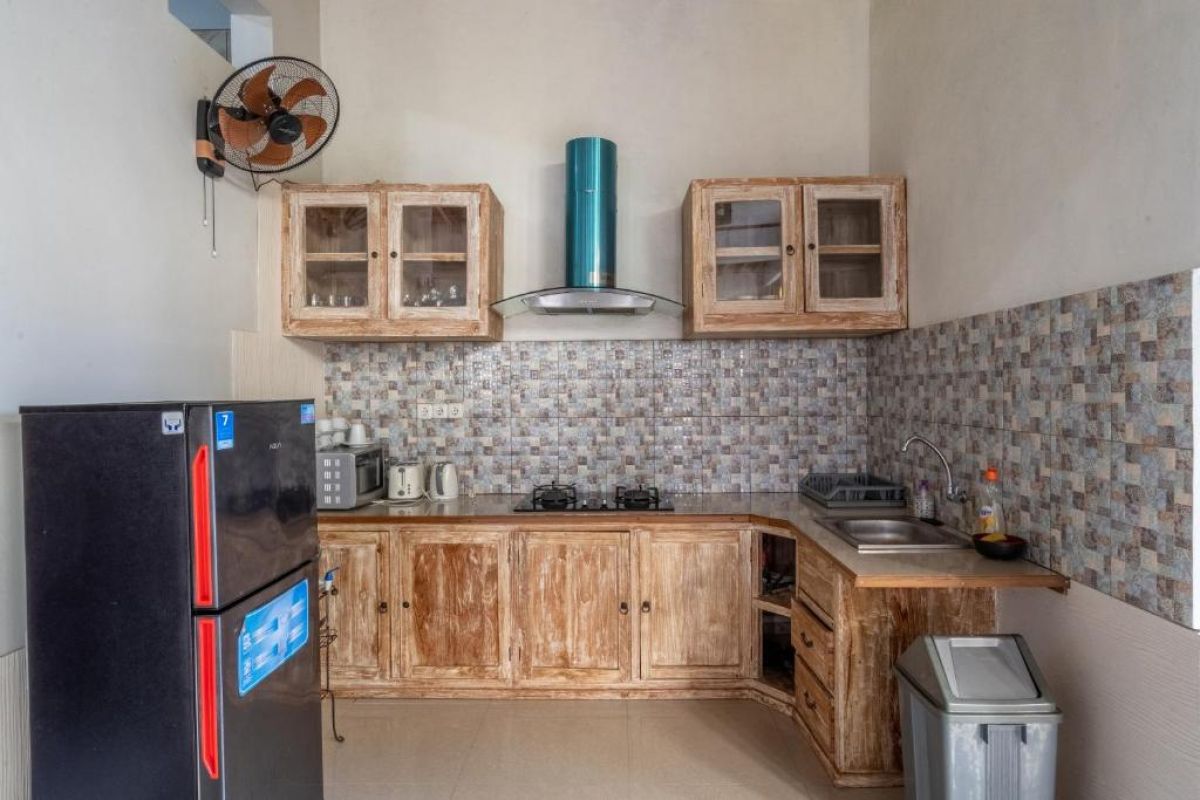 Rustic wooden kitchen with black fridge, gas stove, sink, glass-door cabinets, teal hood, and tiled backsplash. - Bali Villas