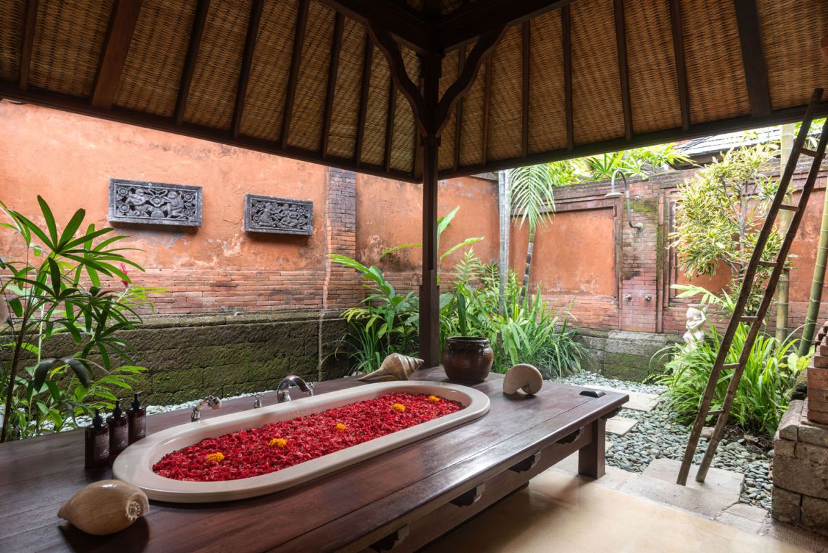 Serene Balinese villa courtyard with koi pond, stone steps, lush tropical plants, and palm trees under a clear sky. - Bali Villas