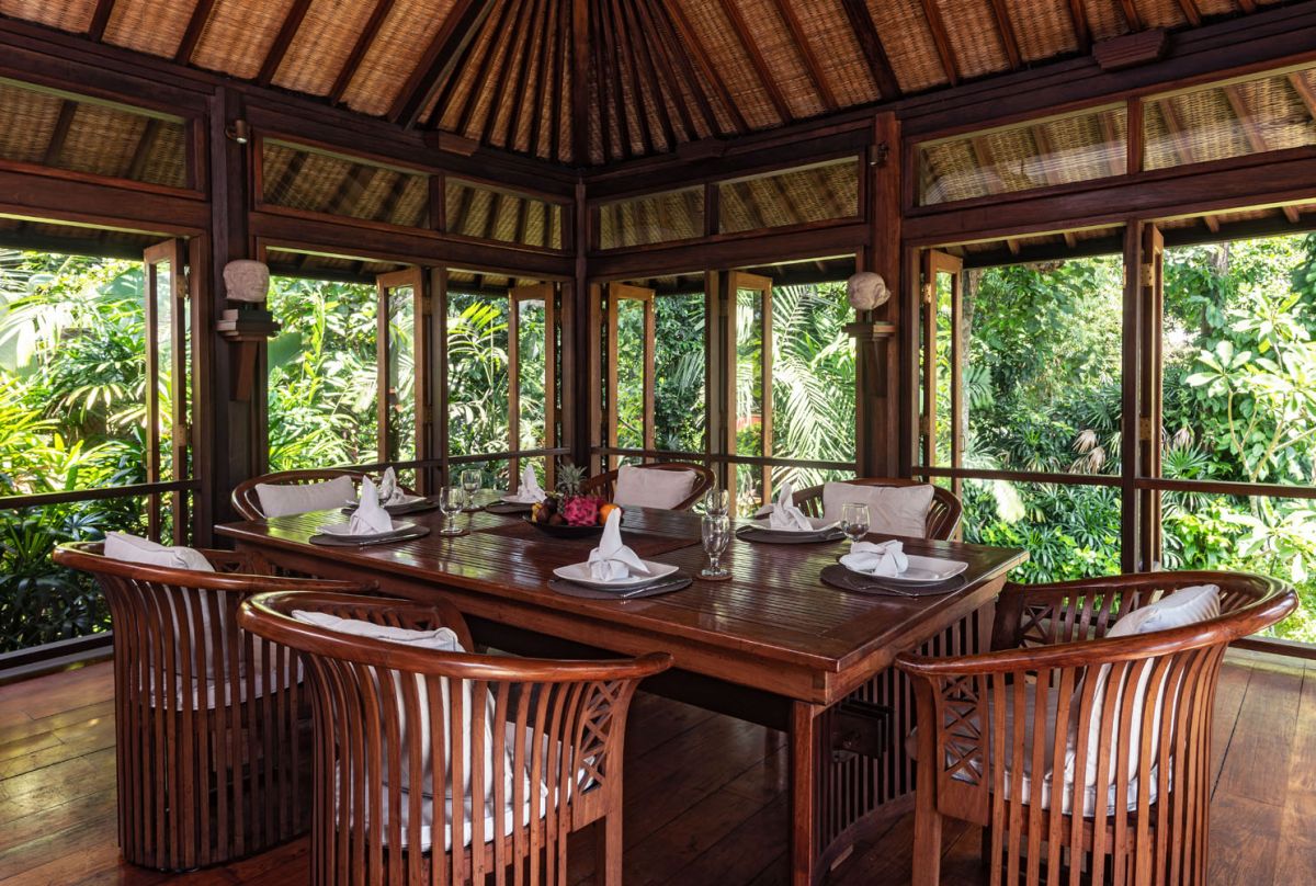 Serene Balinese villa courtyard with koi pond, stone steps, lush tropical plants, and palm trees under a clear sky. - Bali Villas