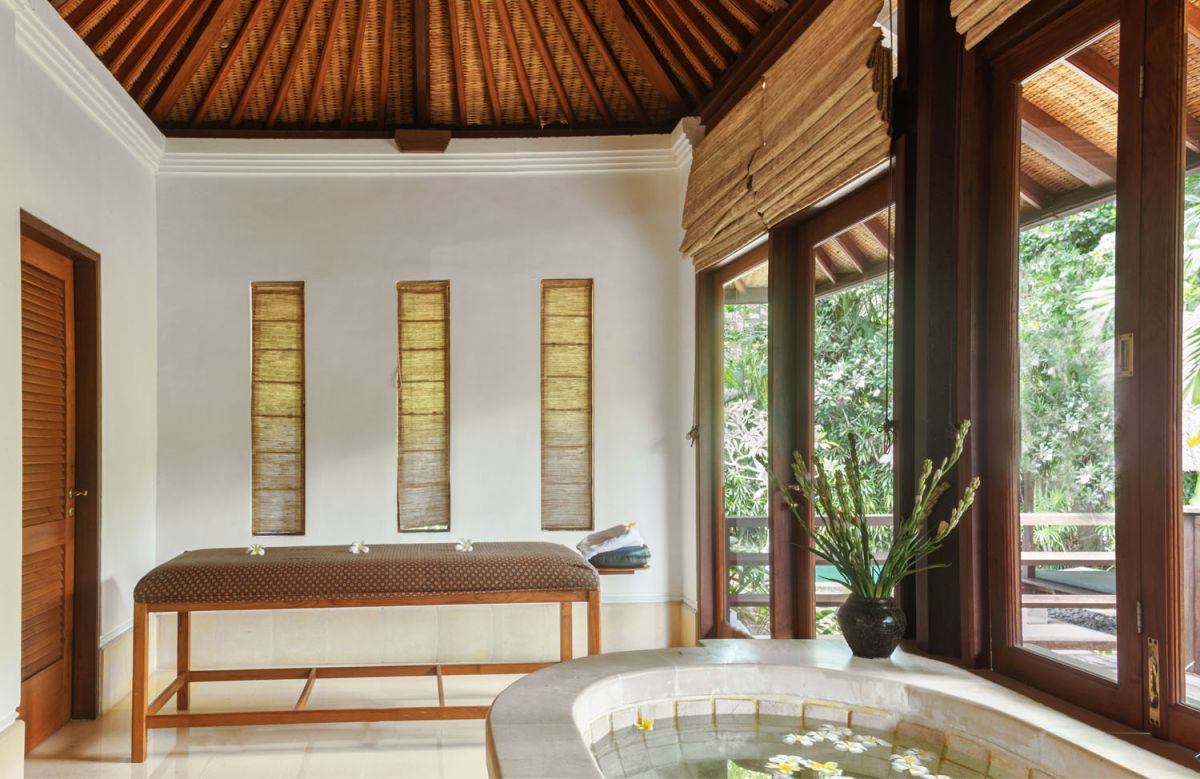 Serene Balinese villa courtyard with koi pond, stone steps, lush tropical plants, and palm trees under a clear sky. - Bali Villas