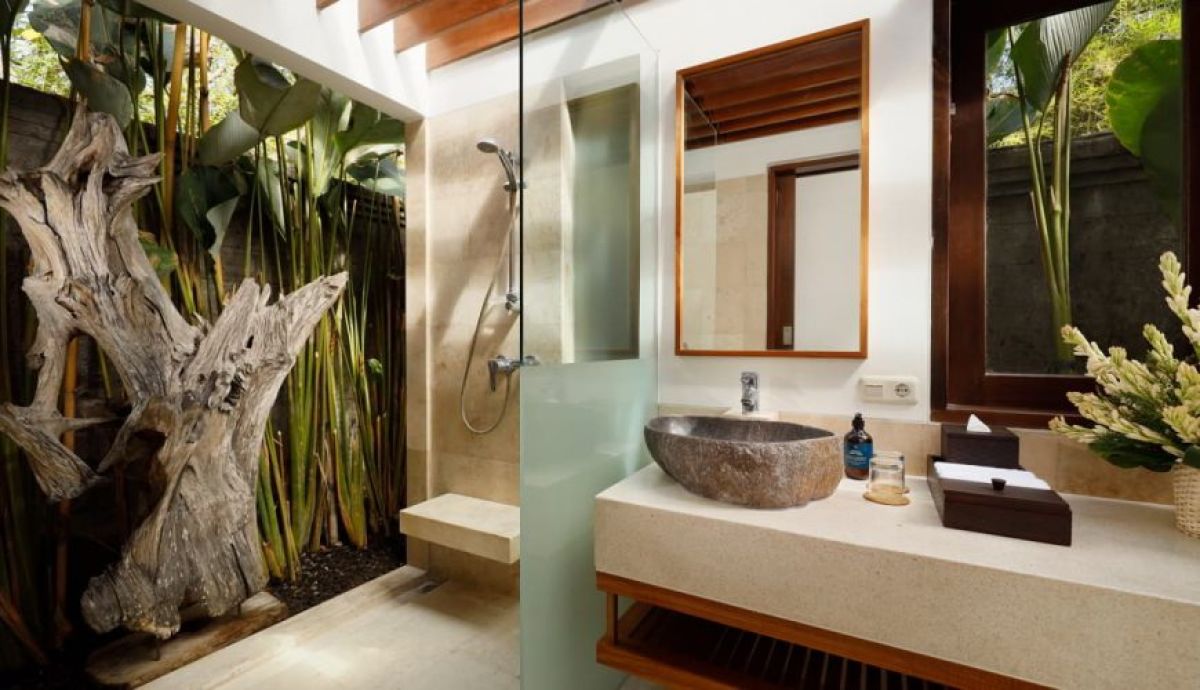 Luxurious tropical Balinese bathroom with stone sink, wooden vanity, open shower, and lush surrounding greenery. - Bali Villas