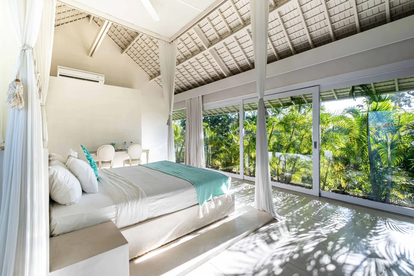 Modern luxury bedroom suite with white platform bed, teal pillow, turquoise sunken bathtub, and garden view through sheer curtains. - Bali Villas