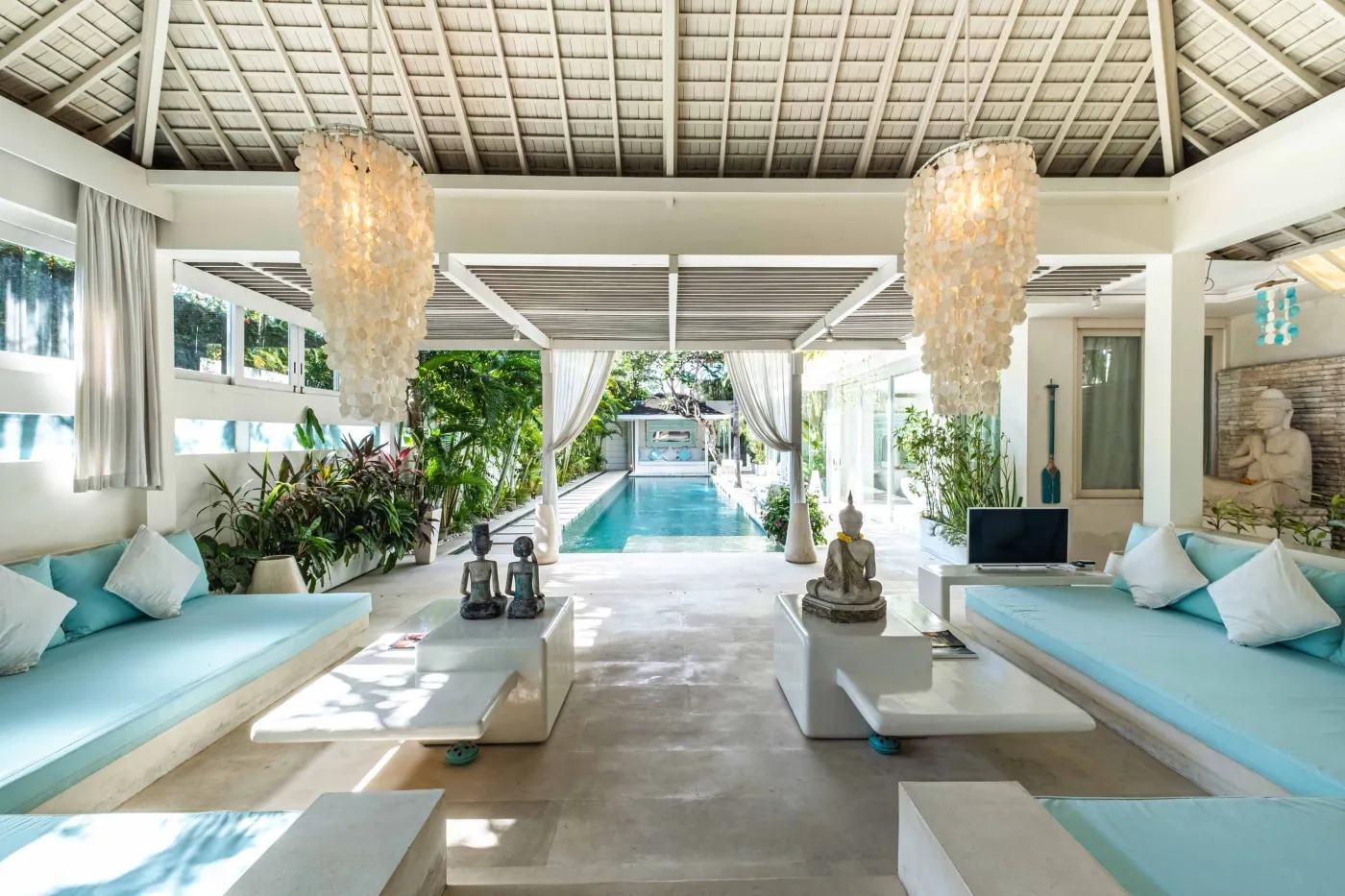 Modern luxury bedroom suite with white platform bed, teal pillow, turquoise sunken bathtub, and garden view through sheer curtains. - Bali Villas
