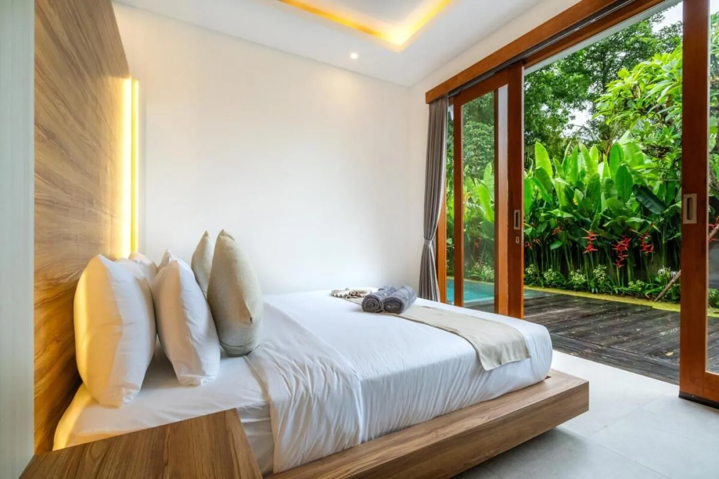 Compact modern bathroom with white toilet, tall potted plant, small shelf of toiletries, and beige walls. - Bali Villas