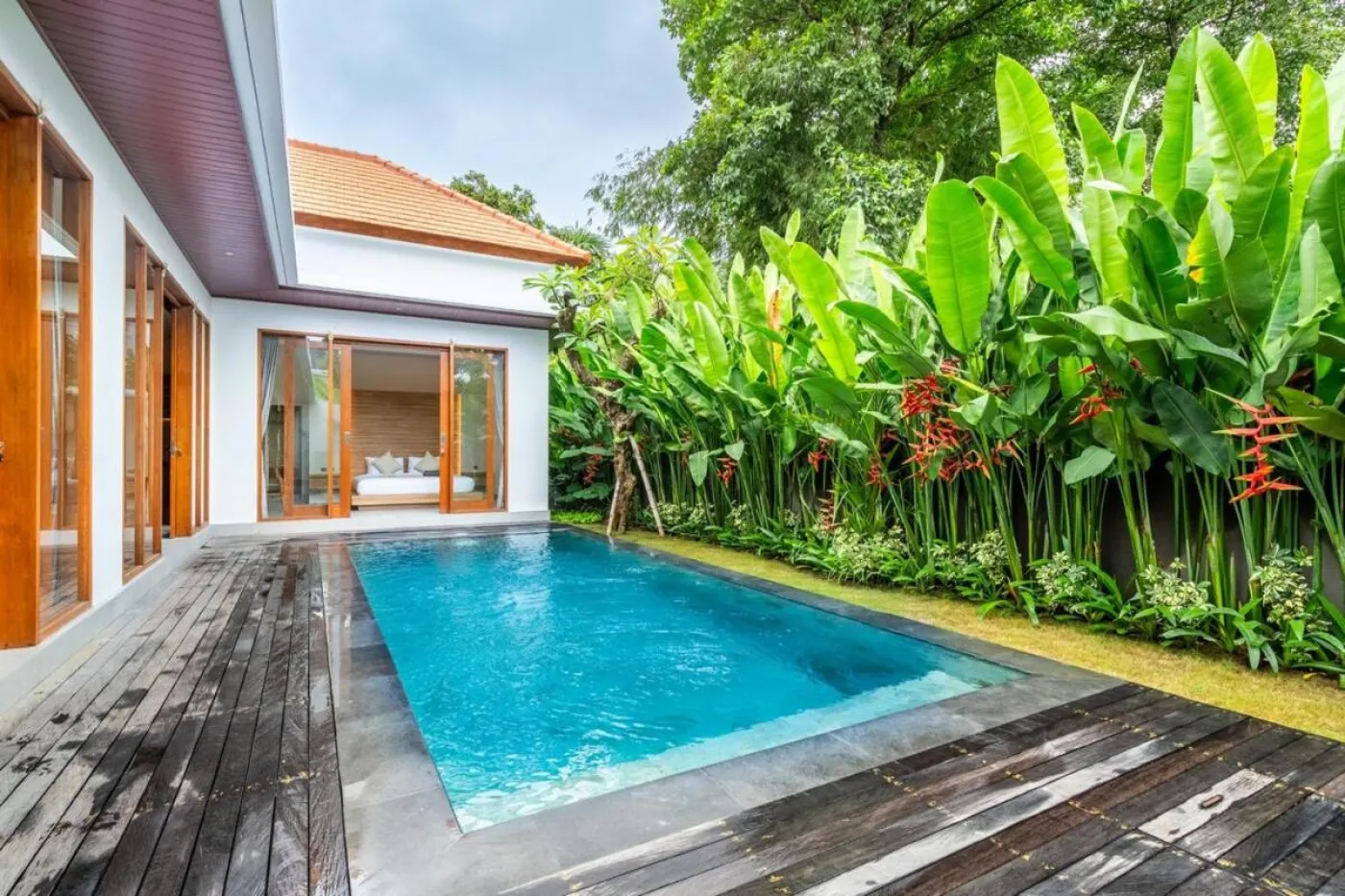 Compact modern bathroom with white toilet, tall potted plant, small shelf of toiletries, and beige walls. - Bali Villas