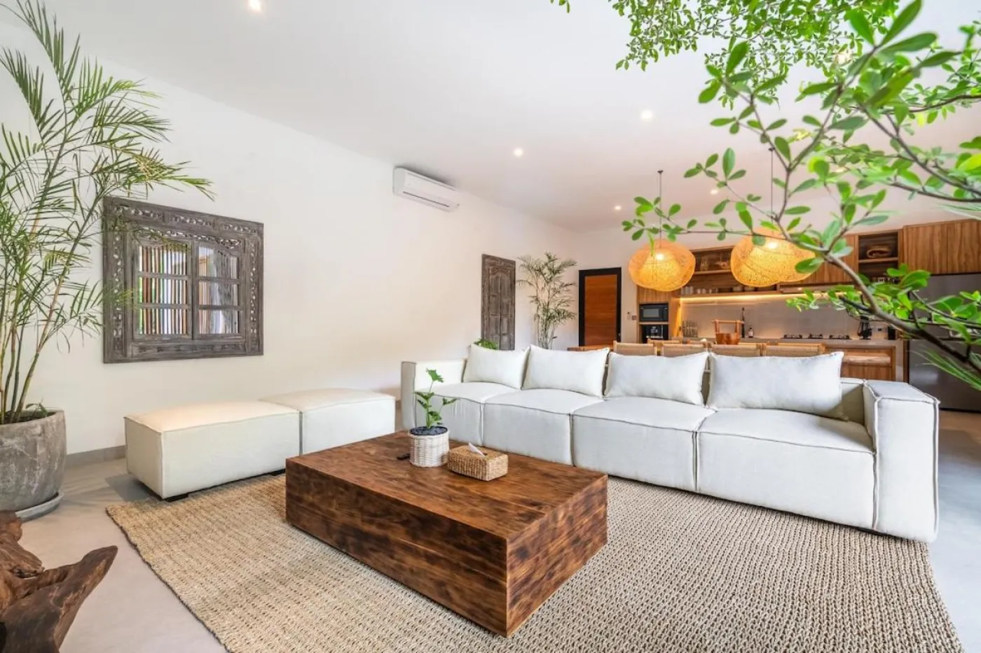 Compact modern bathroom with white toilet, tall potted plant, small shelf of toiletries, and beige walls. - Bali Villas