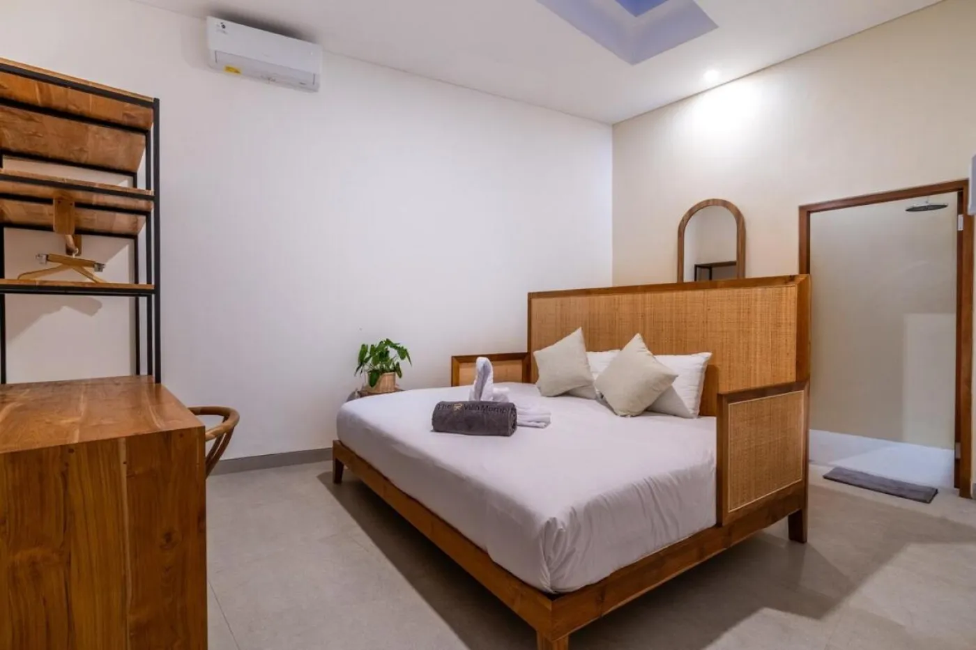 Compact modern bathroom with white toilet, tall potted plant, small shelf of toiletries, and beige walls. - Bali Villas