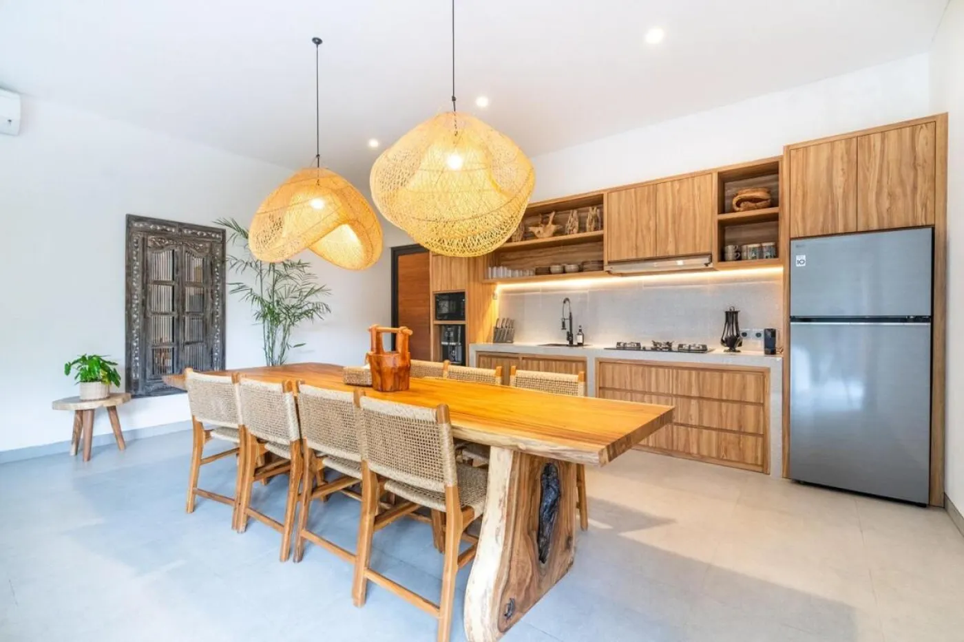 Compact modern bathroom with white toilet, tall potted plant, small shelf of toiletries, and beige walls. - Bali Villas