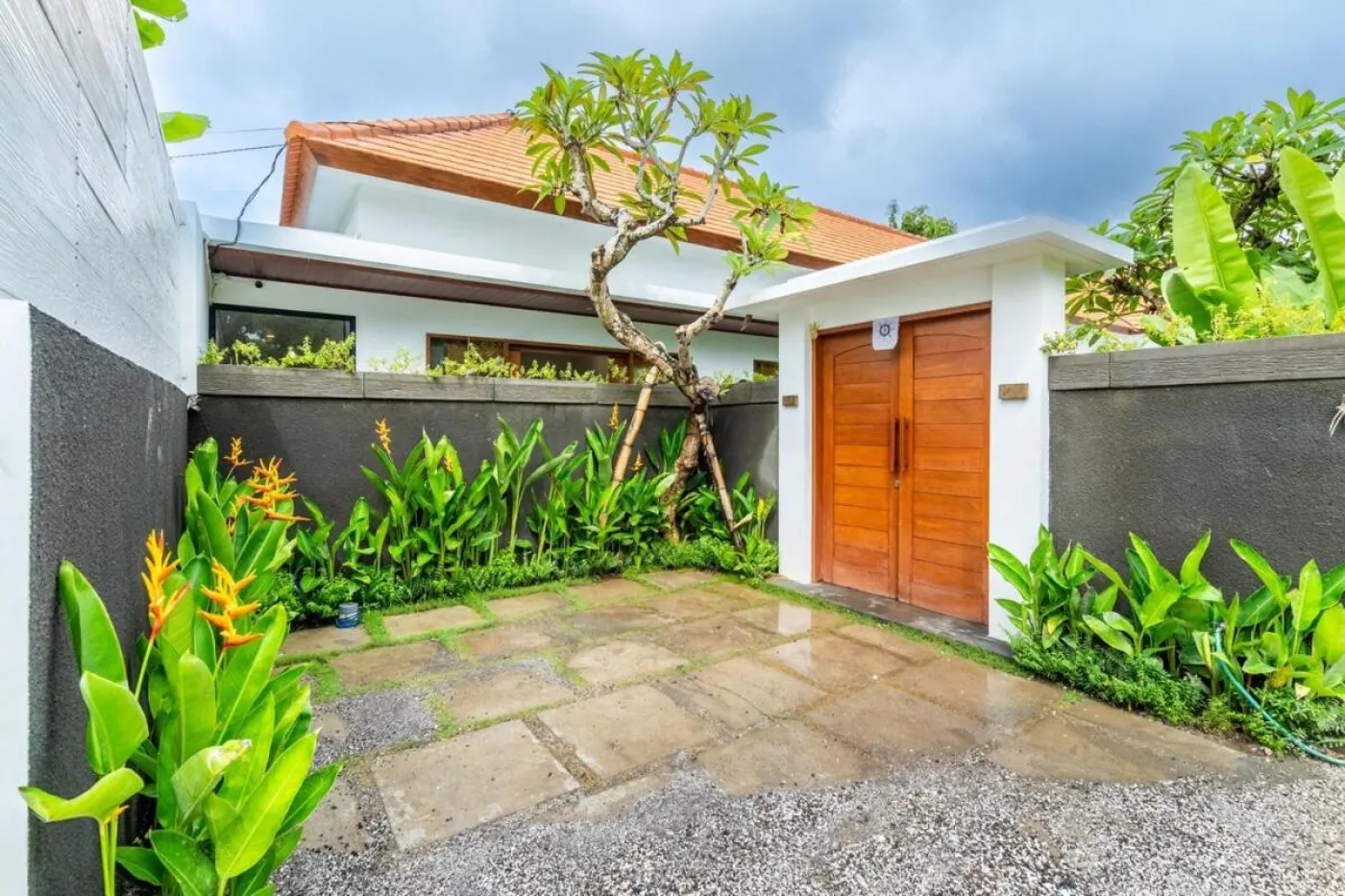Compact modern bathroom with white toilet, tall potted plant, small shelf of toiletries, and beige walls. - Bali Villas