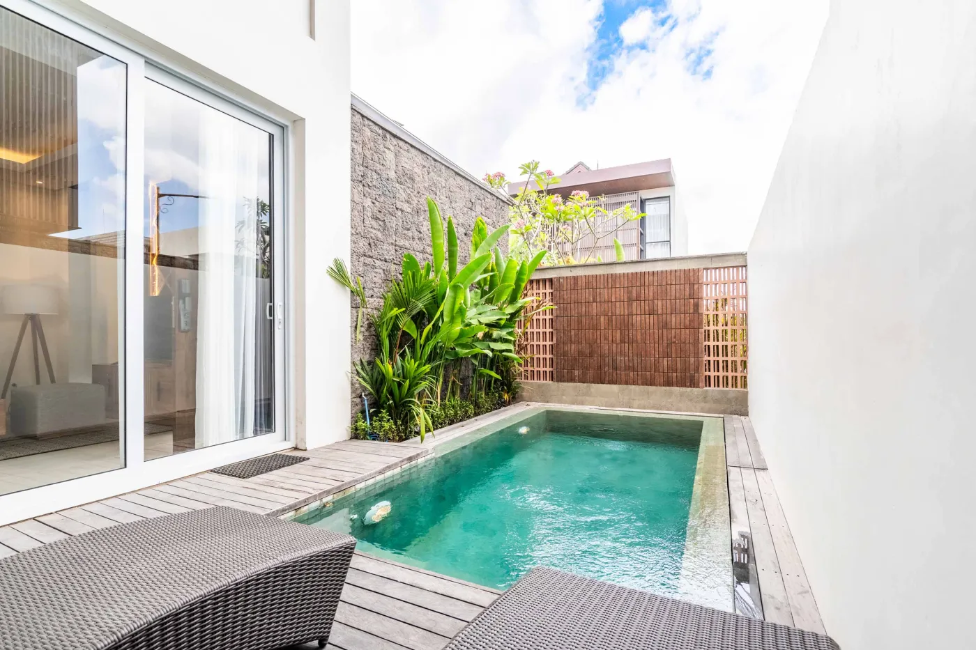 Modern wooden deck balcony with beige sofa, teak table, and chairs, overlooking contemporary rooftops on a sunny day. - Bali Villas