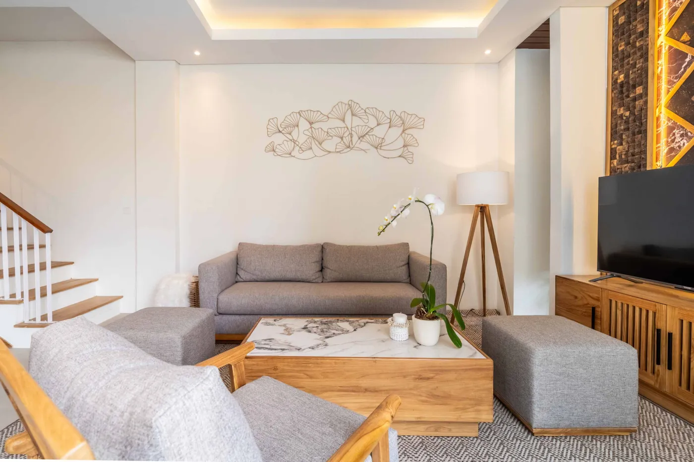 Modern wooden deck balcony with beige sofa, teak table, and chairs, overlooking contemporary rooftops on a sunny day. - Bali Villas