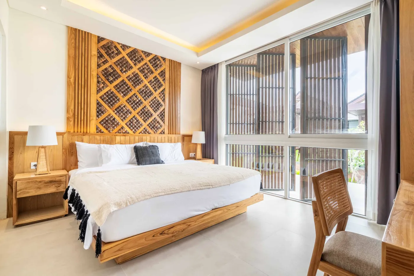 Modern wooden deck balcony with beige sofa, teak table, and chairs, overlooking contemporary rooftops on a sunny day. - Bali Villas