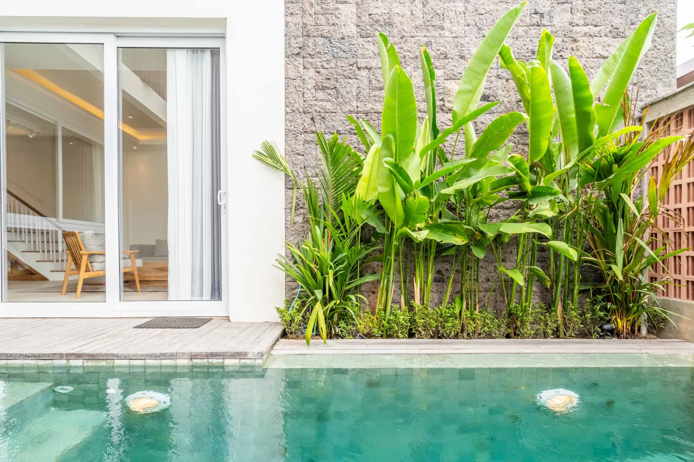 Modern wooden deck balcony with beige sofa, teak table, and chairs, overlooking contemporary rooftops on a sunny day. - Bali Villas