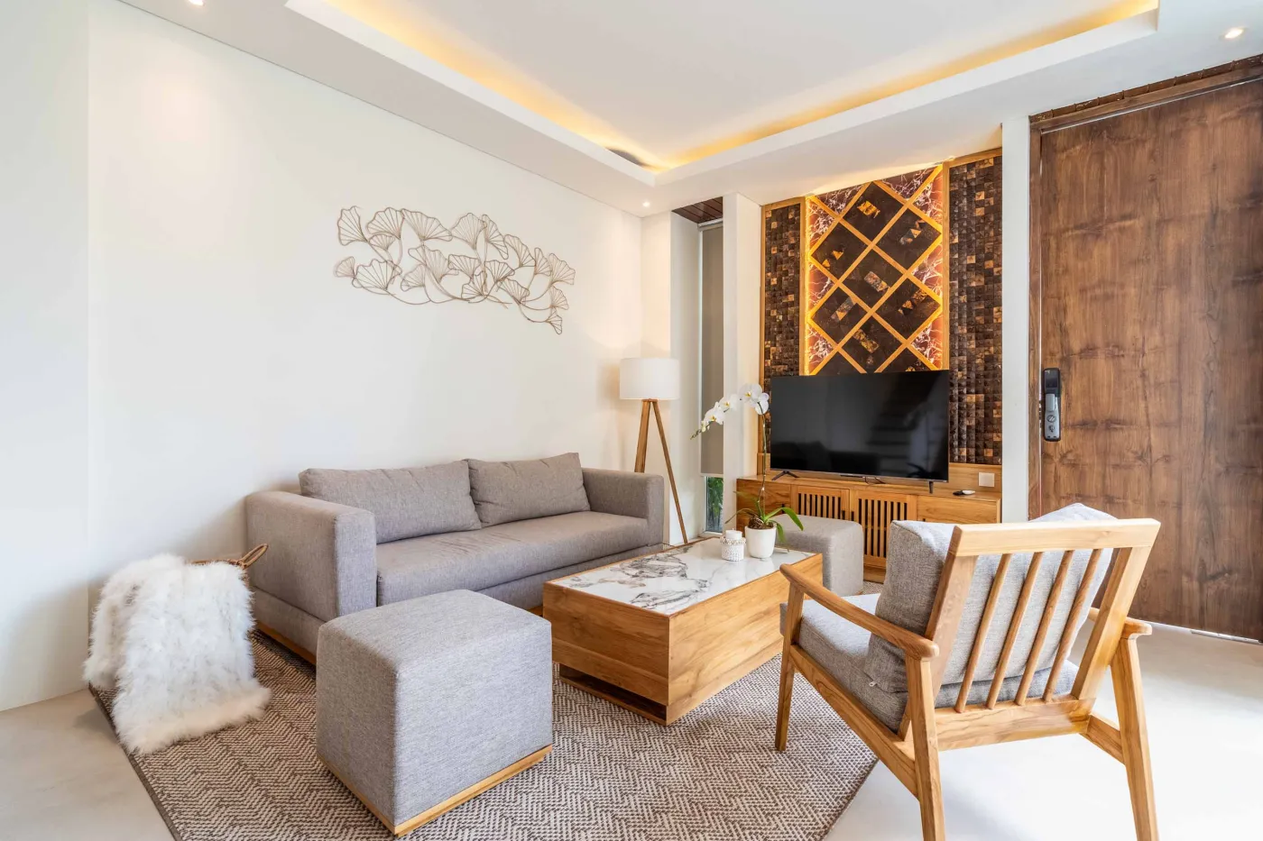 Modern wooden deck balcony with beige sofa, teak table, and chairs, overlooking contemporary rooftops on a sunny day. - Bali Villas