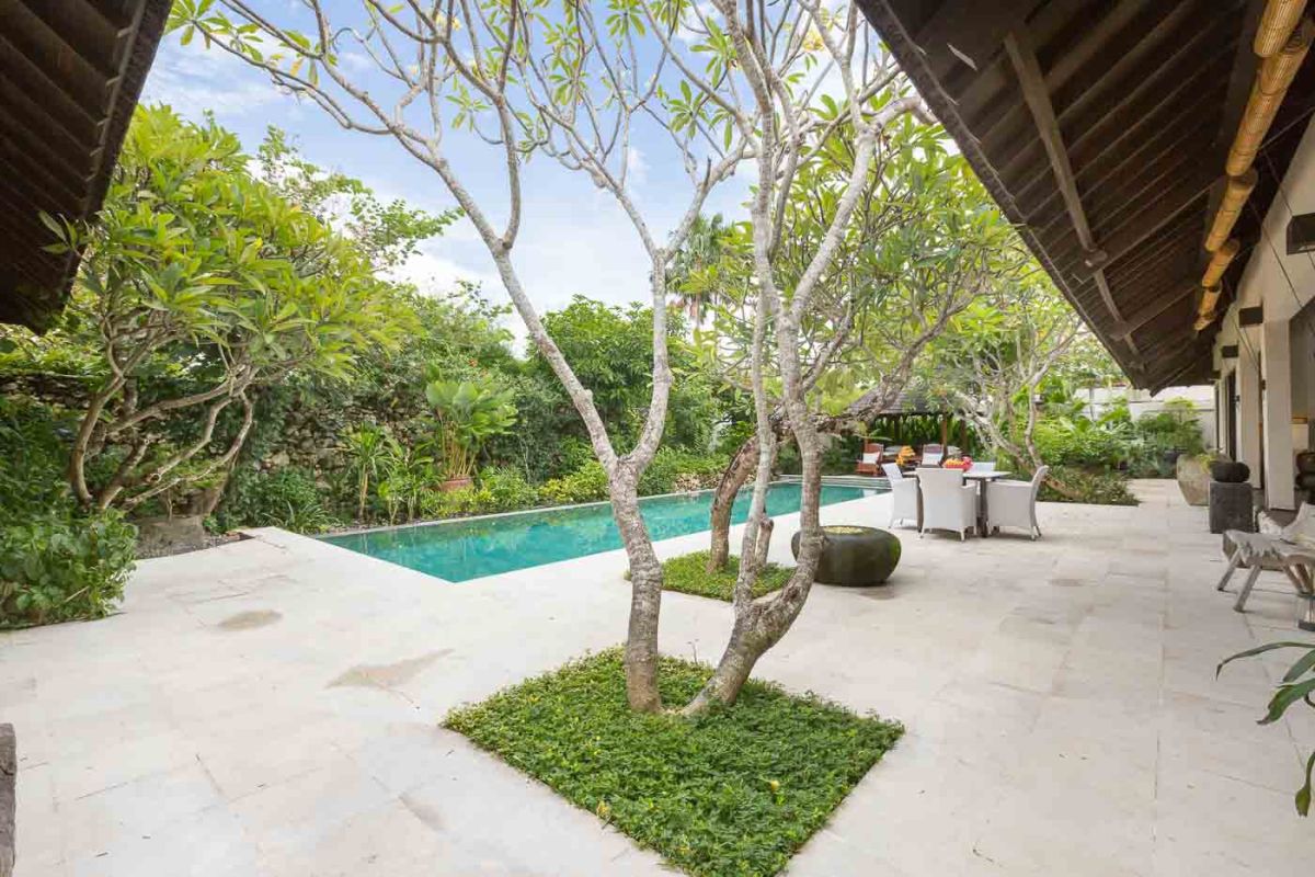 Modern luxury bathroom with freestanding white bathtub, glass shower enclosure, towels, and tropical plant accents. - Bali Villas